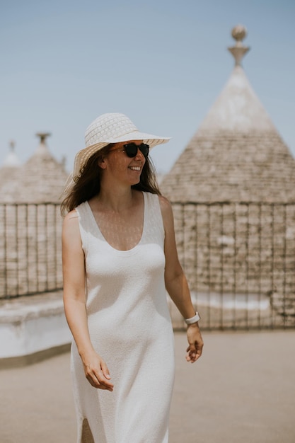 Uma jovem de vestido branco e chapéu em um dia ensolarado durante uma visita turística em Alborebello, Itália