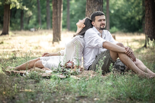 Uma jovem de vestido branco e um homem de camisa estão sentados na floresta na grama, um encontro na natureza, romance no casamento.