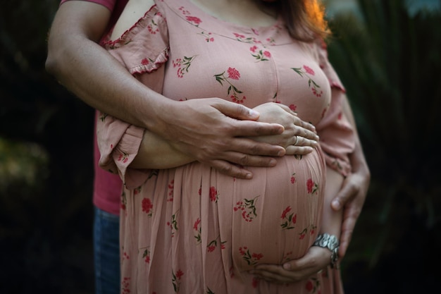 Uma jovem de vestido justo estampado rosa abraça a barriga com um futuro bebê.