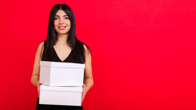 Uma jovem de vestido preto segura duas caixas em um fundo vermelho Presentes para o Dia dos Namorados, Natal e Ano Novo