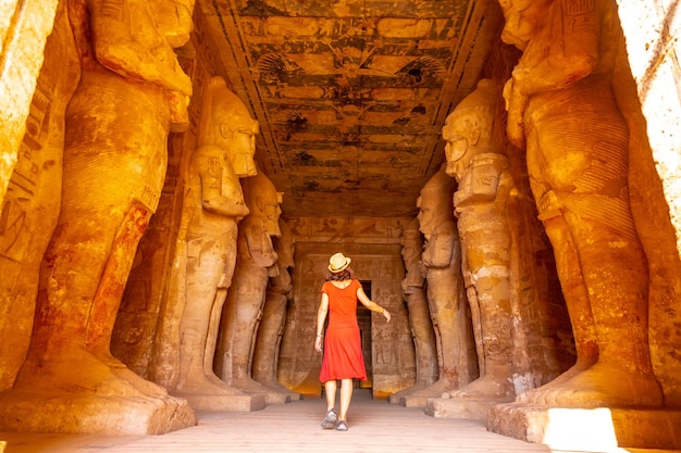 Uma jovem de vestido vermelho no Templo de Abu Simbel ao lado das esculturas