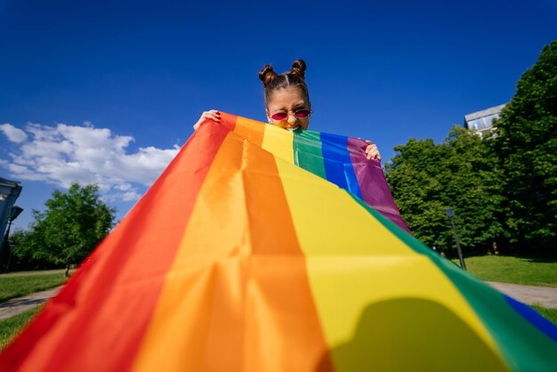 Uma jovem desenvolve uma bandeira de arco-íris contra o céu