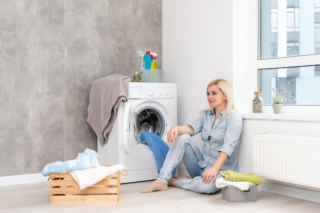 Uma jovem dona de casa com máquina de lavar e roupas. dia de lavar.