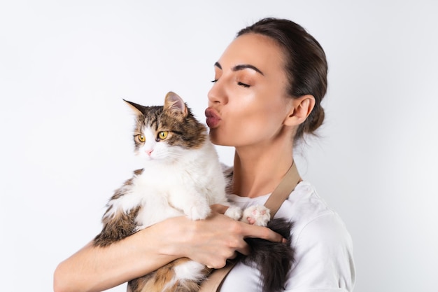 Uma jovem dona de casa de avental sobre fundo branco segura seu amado animal de estimação, um grande gato fofo, uma família feliz