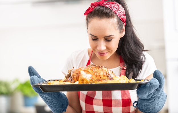 Foto uma jovem dona de casa sente o cheiro de frango assado na hora e batatas em uma bandeja.