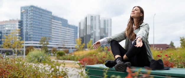 Uma jovem durante uma pausa para o almoço relaxa sentada em uma posição de ioga no parque no fundo de