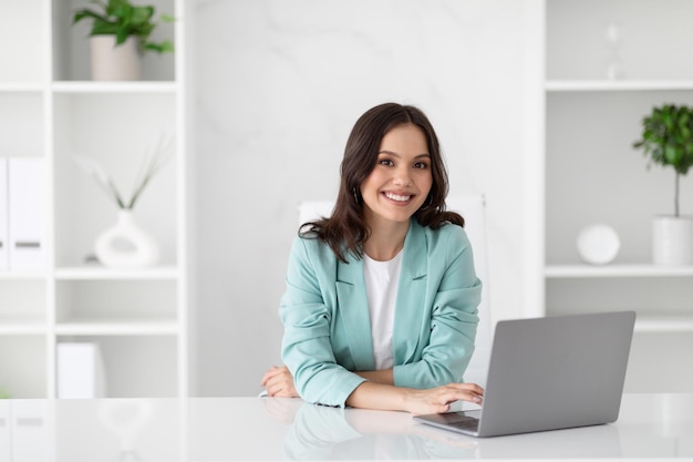 Uma jovem e alegre empresária caucasiana de terno com computador desfruta de ocupação profissional em