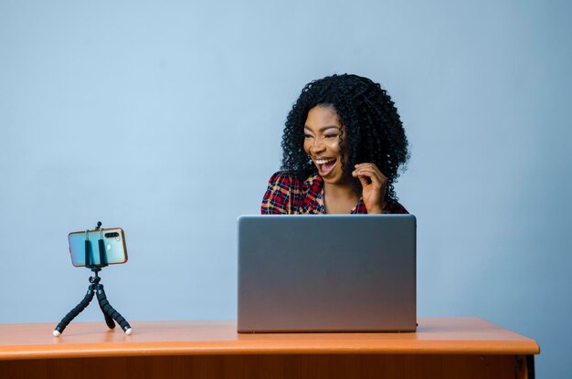 Uma jovem e bela empresária africana isolada sobre fundo branco se sentindo animada enquanto opera seu laptop e faz videochamada com seu celular