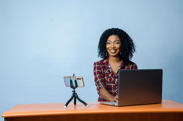 Uma jovem e bela empresária africana isolada sobre fundo branco se sentindo animada enquanto opera seu laptop e faz videochamada com seu celular