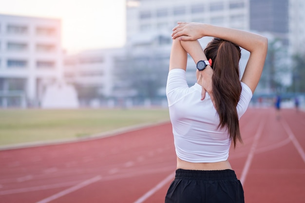 Uma jovem e bela mulher asiática em roupas esportivas, fazendo alongamento antes do treino ao ar livre no parque pela manhã para obter um estilo de vida saudável. Mulher jovem saudável se aquecendo ao ar livre