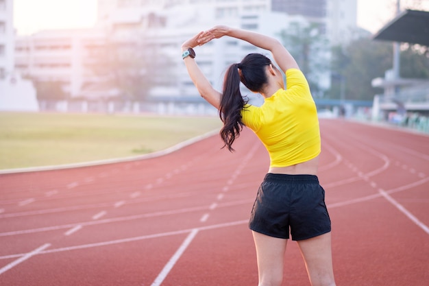 Uma jovem e bela mulher asiática em trajes esportivos, fazendo alongamento antes do treino ao ar livre no estádio da cidade pela manhã para obter um estilo de vida saudável. Jovem saudável fazendo exercícios