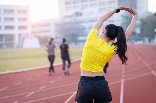 Uma jovem e bela mulher asiática em trajes esportivos, fazendo alongamento antes do treino ao ar livre no estádio da cidade pela manhã para obter um estilo de vida saudável. Jovem saudável fazendo exercícios