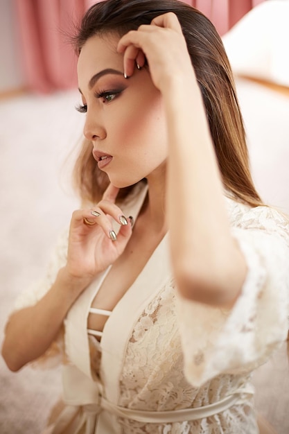 Uma jovem e bela mulher asiática em um roupão de renda bege colocou maquiagem matinal e olha no espelho rasa profundidade de foco foco seletivo