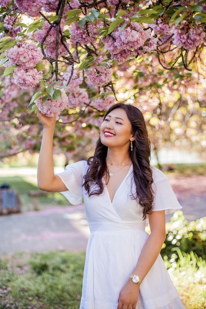 Uma jovem e bela mulher asiática em um vestido branco caminha em um parque florido