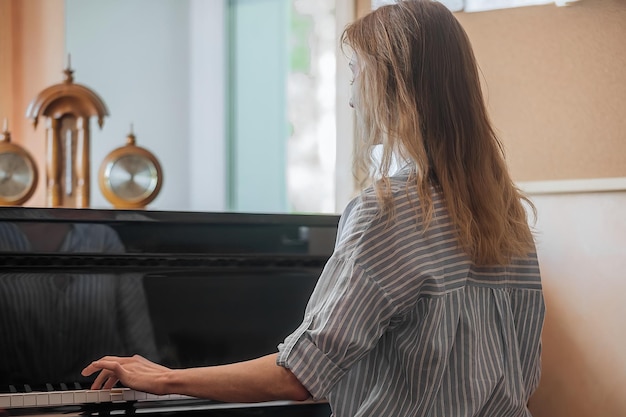 Uma jovem e bela mulher senta-se de costas para nós e toca piano, aulas de música em jovens