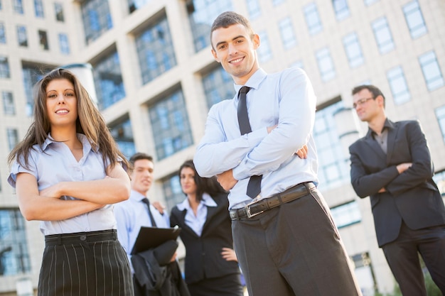 Uma jovem e bonita empresária e empresário com sua equipe no fundo em pé na frente da empresa, olhando para a câmera e sorrindo.