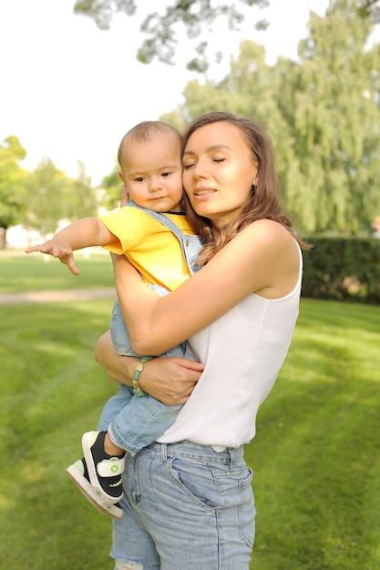 uma jovem e linda mãe abraça seu filho pequeno em uma camiseta amarela e jeans no parque