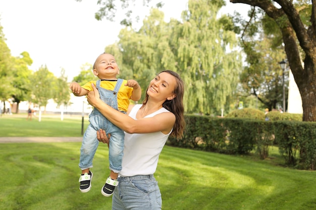 uma jovem e linda mãe abraçando seu filho pequeno em uma camiseta amarela e jeans no parque