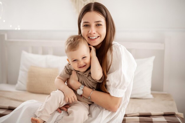 Uma jovem e linda mãe com um menino abraçando-se na cama em casa no quarto cuidando e amando crianças e pais