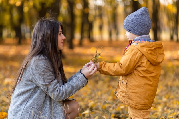 Uma jovem e linda mãe passa um tempo em uma caminhada com seu amado filho no parque de outono