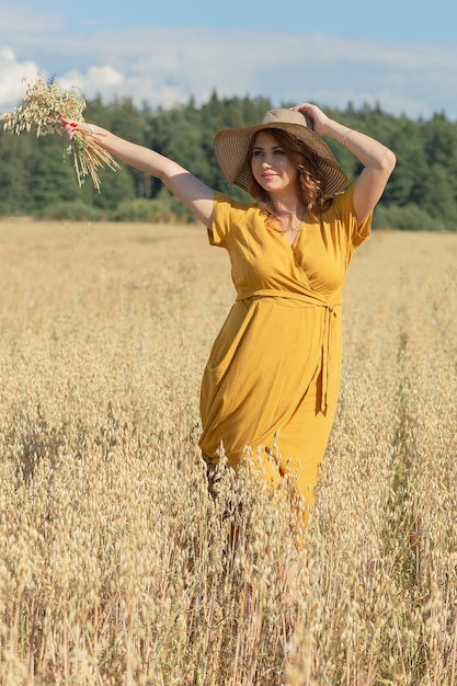 Uma jovem e linda mulher grávida com um vestido e chapéu amarelo caminha por um campo de trigo laranja em um dia ensolarado de verão