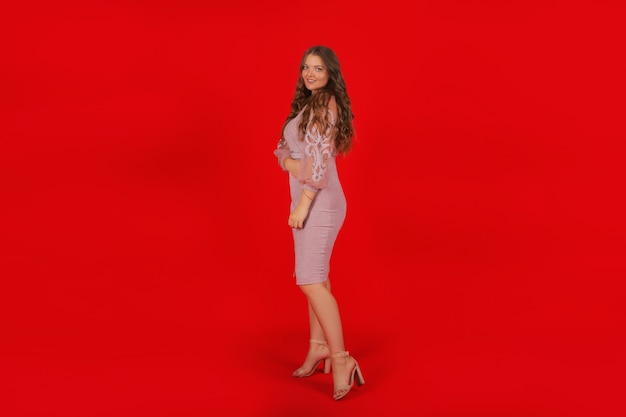 uma jovem elegante alta linda garota com cabelo comprido em um vestido rosa festivo sobre um fundo vermelho