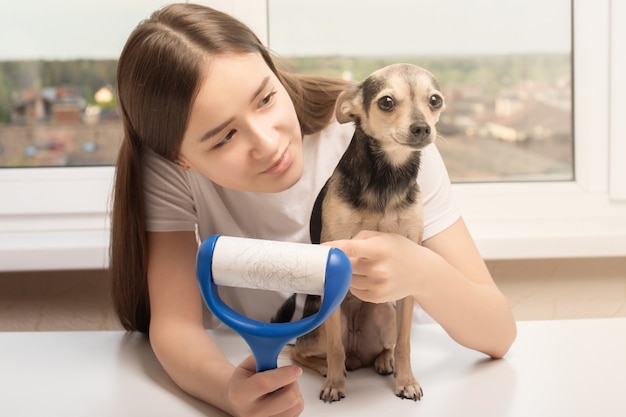 Uma jovem em casa repreendendo um cachorro por causa da lã, mostrando um rolo para limpar