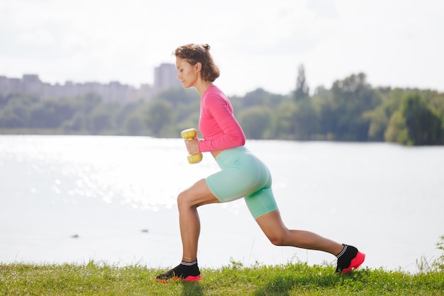 Uma jovem em roupas brilhantes pratica esportes em um parque na natureza