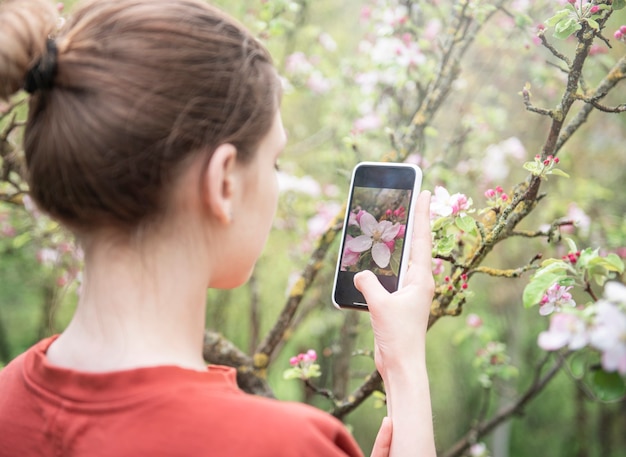 Uma jovem em um jardim florido tira fotos de árvores floridas em um smartphone