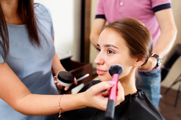 Uma jovem em um salão de beleza com um cabeleireiro e maquiador