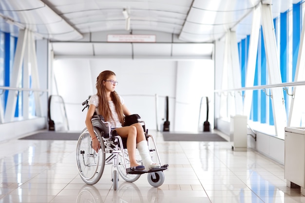 Uma jovem em uma cadeira de rodas está de pé no corredor do hospital.