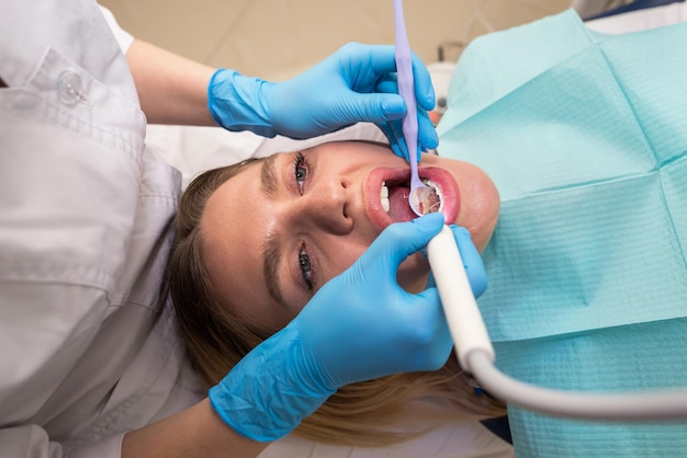 Uma jovem em uma cadeira odontológica enche um dente Visitando um ortodontista O processo de remoção da placa dos dentes Tratamento odontológico em uma clínica odontológica