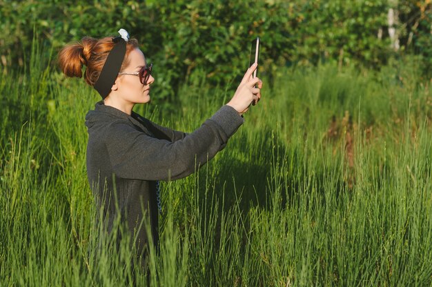 Uma jovem em uma clareira perto da floresta se comunica em uma teleconferência em um tablet.