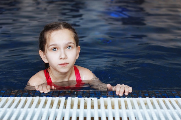 Uma jovem em uma piscina com água azul olha para a câmera