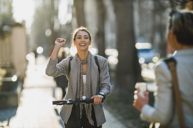 Uma jovem empresária andando de scooter elétrica e cumprimenta alguém a caminho do trabalho.