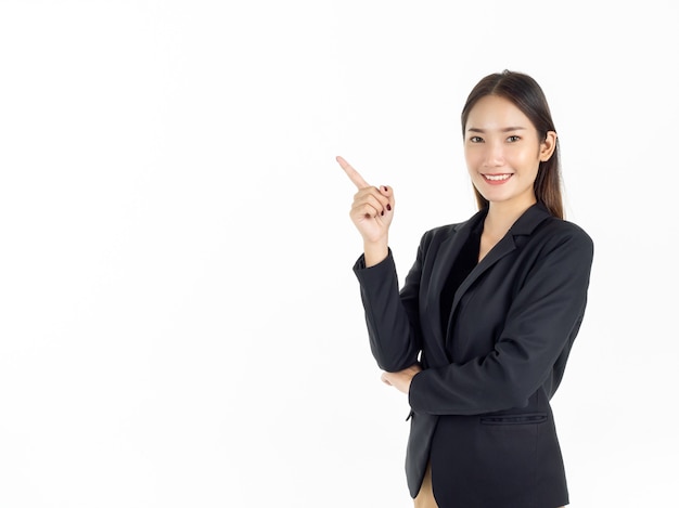 Uma jovem empresária asiática atraente em um terno preto apontando o dedo para apresentar no espaço da cópia e olhando a câmera com um sorriso dentuço