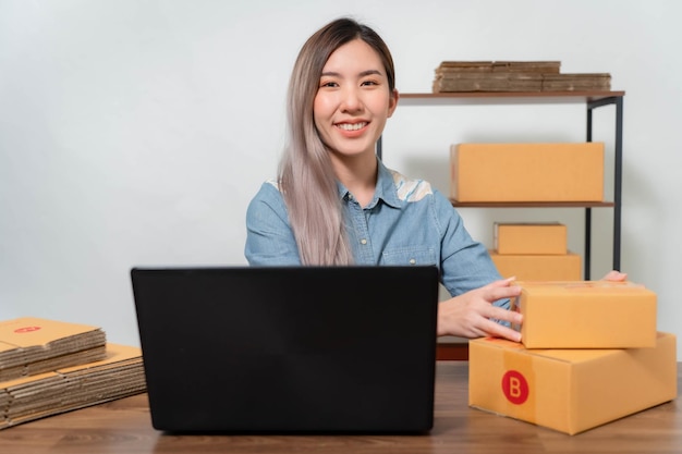 Uma jovem empresária está muito feliz depois de verificar seu e-mail através de seu laptopVendedores on-line estão embalando produtos em caixas de encomendas