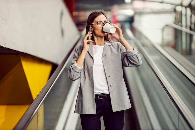 Uma jovem empresária ocupada está descendo a escada rolante e tomando seu café