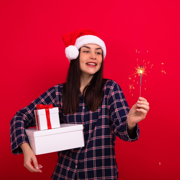 Uma jovem encantadora de pijama segura caixas de presentes e estrelinhas em um fundo vermelho noite de natal em casa