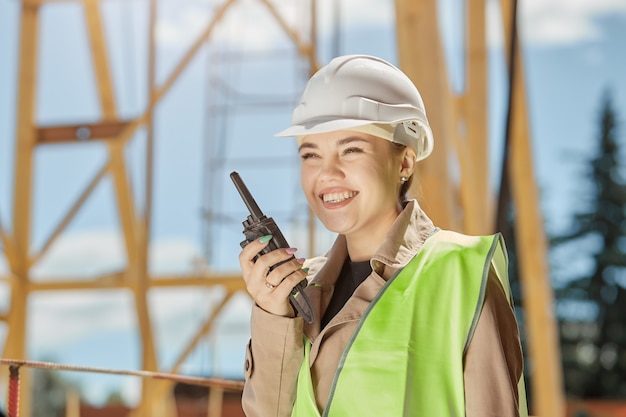 Uma jovem engenheira civil no setor de construção civil se comunica pelo walkie-talkie com um sorriso no rosto