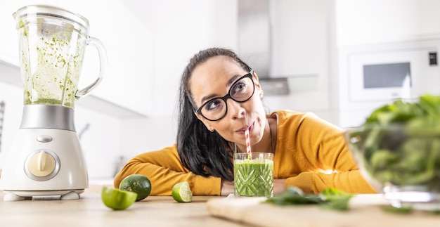 Uma jovem engraçada bebe um smoothie verde que ela mesma fez