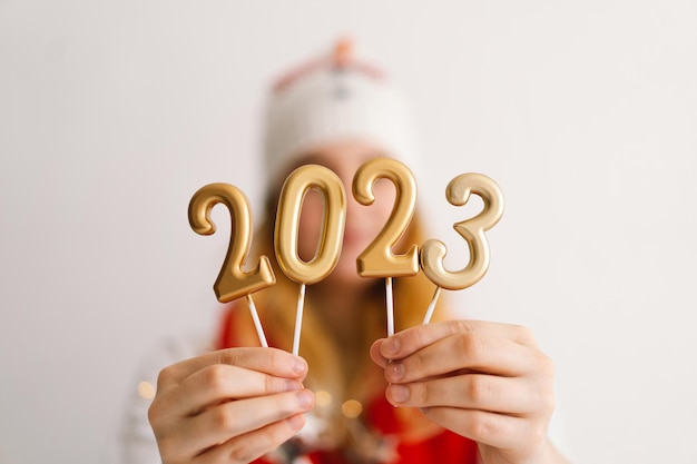Foto uma jovem engraçada com um chapéu de ano novo e um lenço vermelho segura os números 2023 nas mãos.