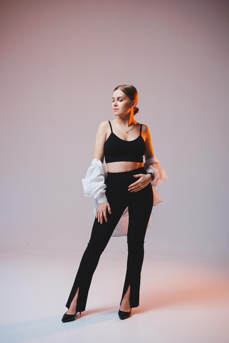 Uma jovem esbelta em uma camisa branca e calça preta com maquiagem no rosto posa em um fundo liso Mulher europeia elegante em um top preto
