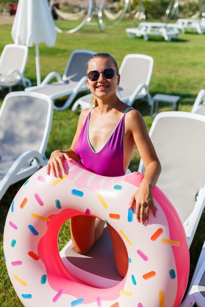 Uma jovem esguia segura um círculo inflável nas mãos, de pé na grama verde. Modelo atraente com corpo perfeito. Conceito de férias, garota vai nadar no mar