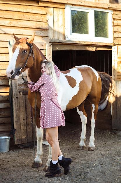 Uma jovem está acariciando e sorrindo seu cavalo no estábulo em uma fazenda rural