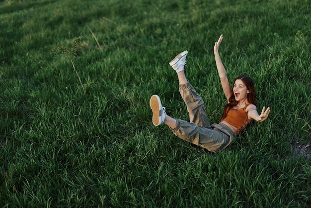 Uma jovem está brincando no parque conosco na grama e cai no chão sorrindo feliz ao sol Descansando na natureza harmonia com o corpo