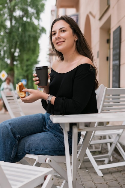 Uma jovem está comendo um croissant e bebendo café café da manhã de verão lá fora