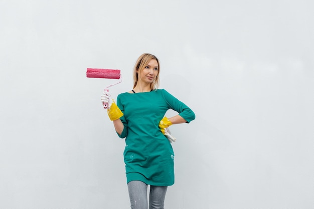 Uma jovem está consertando uma parede branca e sorrindo com um rolo rosa nas mãos