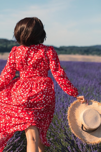 Uma jovem está correndo em um campo de lavanda e segurando um chapéu de palha