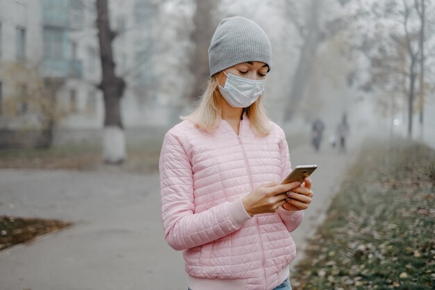 Uma jovem está de pé perto da estrada com uma máscara médica. Proteção contra uma epidemia de vírus em uma cidade no inverno.
